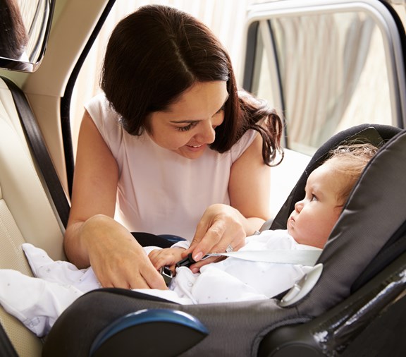 Mother Putting Baby Son into Car Travel Seat