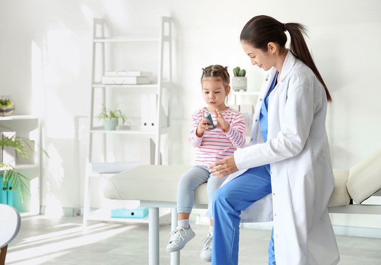 Female pediatrician and cute little girl with inhaler in clinic