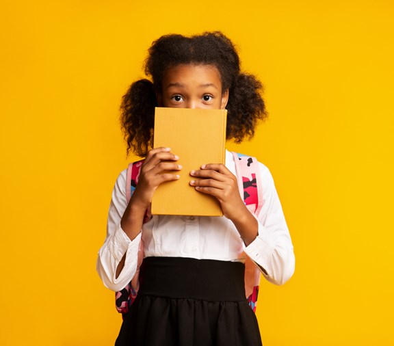 Young girl worried about school and covering her face with a notepad