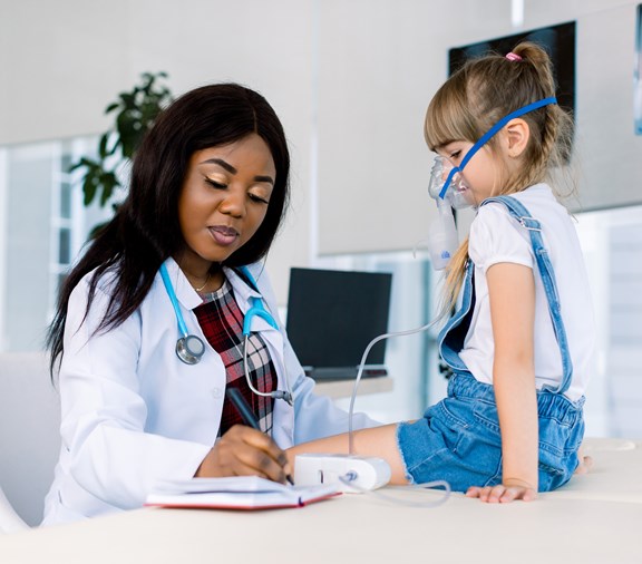 Young African female Doctor helping to little girl with nebulizer mask. Medical doctor applying medicine inhalation treatment on a little girl with asthma inhalation therapy by the mask of inhaler.