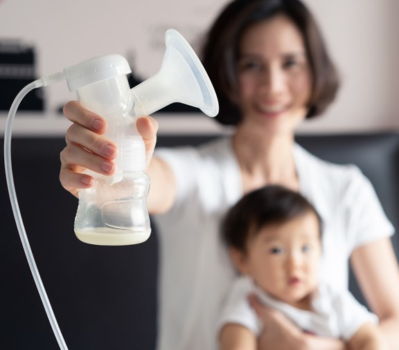 mother holding breast pump milk on the bed in bedroom. Mother hugging her little cute baby in arm and feeling happy expression on face. Breast Pumping milk concept.
