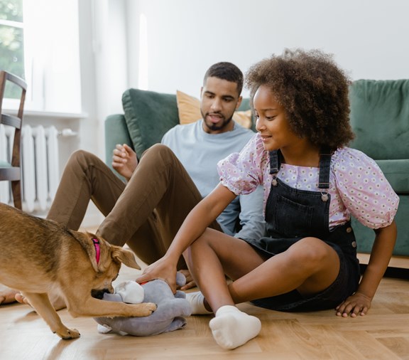 little girl playing with dog while dad watches over