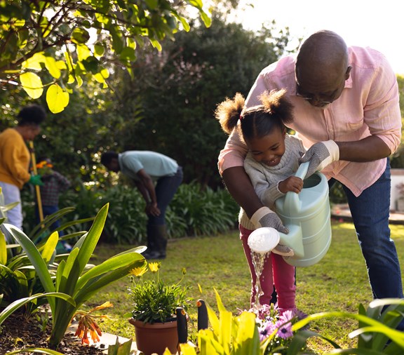 Happy african american man and his granddaughter watering plants in summer garden